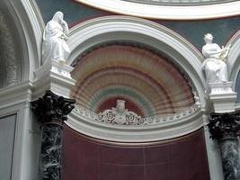 Multicolored arch in shape of seashell flanked by statues of woman in robe and man playing harp