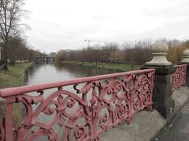 View of river spree from bridge. Reddish metal railing with fleur-de-lis pattern in foreground