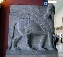 Black stone sculpture of creature with head of bearded human, body of lion, and wings.