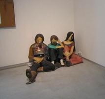 Three figures seated in corner, also have loudspeakers for faces