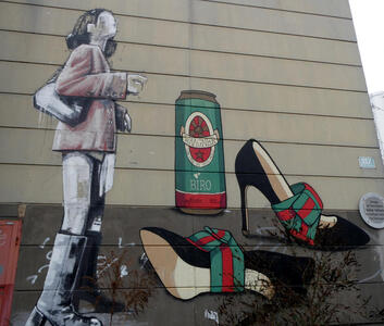 Woman standing next to high-heeled shoes and a beverage can with the slogan “Low Life in High Heels} and the name of the street (Waagner-Biro)