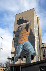 Multi-story painting of man in orange t-shirt and blue jeans with head of a bull.