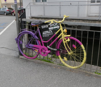 Bicycle painted in purple, magenta, and yellow with advert for Bike Shop Lemur