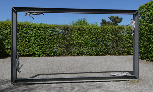 Large empty metallic picture frame with human figures along the frame’s inner edges.