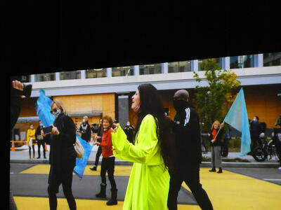 Woman in yellow robe with black hijab walking down street, yelling.