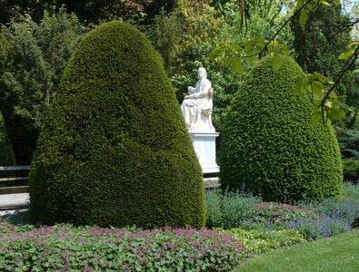 Statue between two roughly conical bushes.