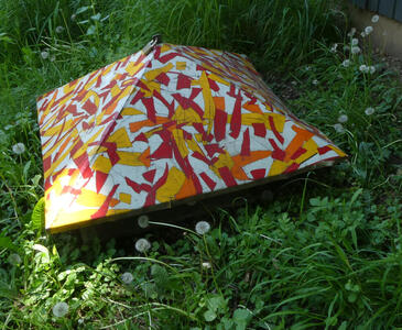 Utility cover decorated with orange, red, and yellow geometric shapes.