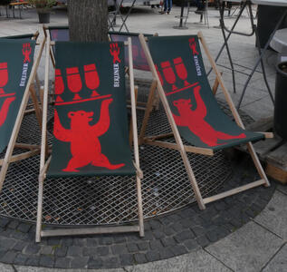 Red colored bear holding a try with three beer glasses above his head.