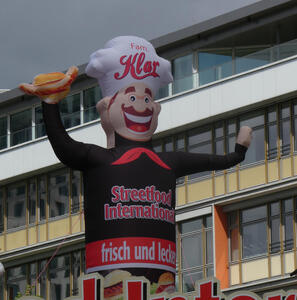 Inflated man with moustache in chefs hat with waving arm.