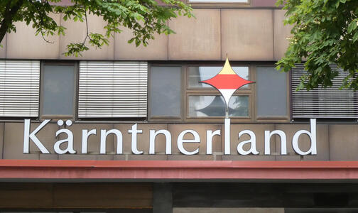 Logo for Kärtnerland, a housing project. logo has a diamond with yellow, red, and white horizontal stripes.