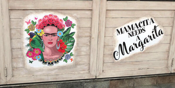 Mexican-style painting of Frida Kahlo. Next to it, a sign reading “Mamacita needs a Margarita”