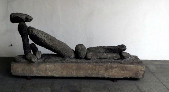 Sculpture of man lying on his side. It is made of several individual stones
