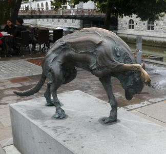 Bronze sculpture of an animal with one front paw raised off ground