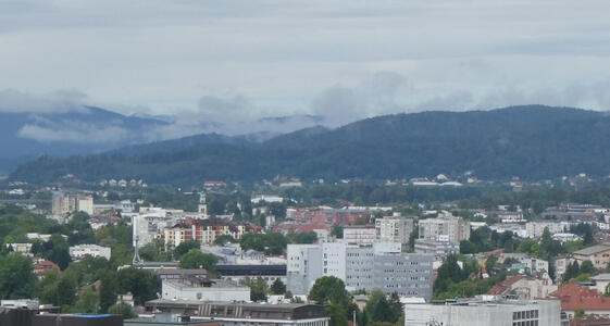 View of city with mountains in background; clouds are floating at low height on mountain