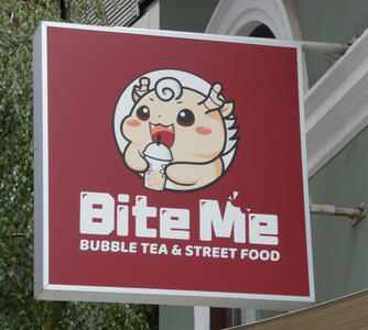 Cartoonish character drinking bubble tea. Sign reads “Bite Me / Bubble Tea & Street Food”