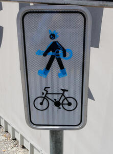 Traffic sign with pedestrian symbol spray-painted to resemble a person with a mohawk carrying a guitar and wearing rollerblades