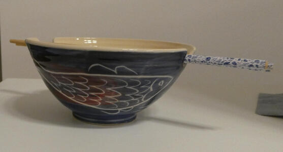 Blue bowl with fish drawn on side. Top of bowl has indentations for chopsticks to rest in.