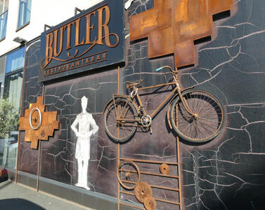 Exterior of Butler Restaurant and Bar with a rusted-looking bicycle frame attached to the wall. Also on the wall is a drawing of a butler holding a tray.