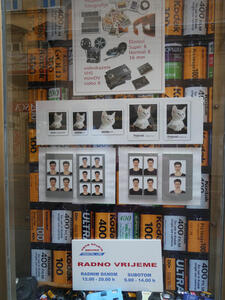 Window of a photography store featuring transfer-to-disk services, varying sizes of photos (with a picture of a cute cat), and rolls of film.