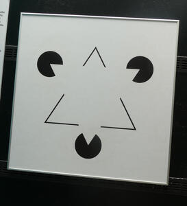 An illusory triangle; three circles at the vertices of a “triangle“ have triangular segments cut out of them, creating the illusion of a solid white triangle.