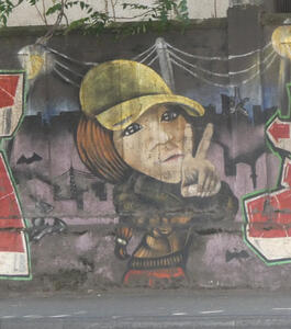 Person with long hair and yellow baseball cap, making a V (peace sign)