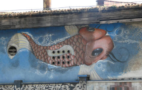 Painting of a fish. Holes in the wall align with the fish’s scales.