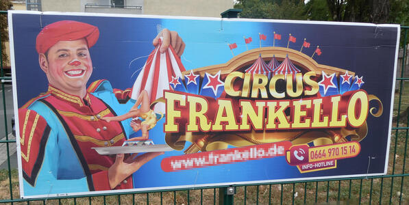 Grinning circus clown holding a platter, on which is a female contortionist, resting with her elbows on the ground and her legs pointing the same direction as her head. The clown holds a red-and-white circus tent in his other hand.