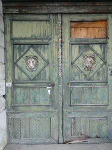 Green wooden doors. On each door is a diamond with a lion’s head reliefwork
