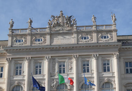 Upper floors of a palace. At the bottom of the photo are EU, Italy, and Trieste flags.