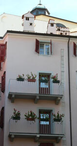 Balconies on two upper stories of a building; both have planter boxes with flowers in them.