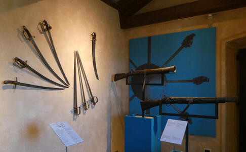 Display with swords on one wall, blunderbusses on other wall