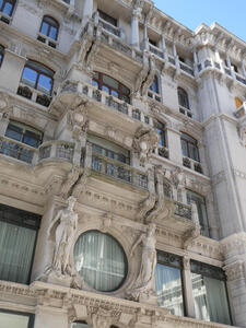 Multi-story building with ornate decorative sculpture and a round window on the first floor above ground