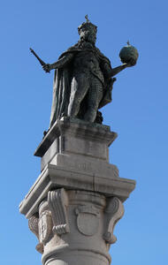 Statue of man wearing crown. He has a short sword in one hand and a cross-topped orb in the other