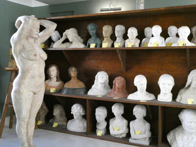 At left, full-sized statue of naked woman. In center and right, three shelves of busts of a variety of people.