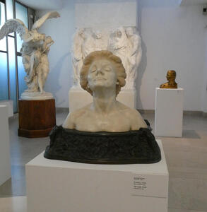In foreground, bust of a woman, smiling, with her head tilted slightly upwards. Her hair is painted blonde.