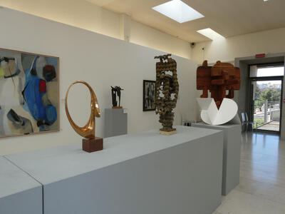 View of room with several abstract sculptures, one of them a gold hoop-shaped piece