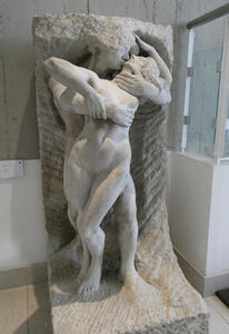 Sculpture of man and woman kissing. The man’s head and arm emerge from the stone slab at the back