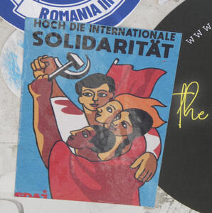 Group of people holding hammer and sickle; red flag in background. Text: Hoch die internationale Solidarität