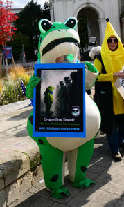 Person in inflatable frog costume holding a sign for “Oregon Frog Brigade”