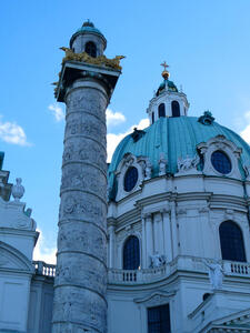 Ornately carved column with gold filligree at top in front of a church dome.
