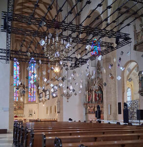 Interior church with mirrored diamond shapes hanging from ceiling. In background, stained glass windows.