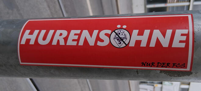 Hurensöhne; the O is a symbol of some soccer team? with a diagonal slash through it.
