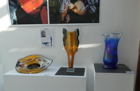 From left to right, an orange plate, an abstract orange sculpture, and at right a vase that is primarily blue but clear at the top.