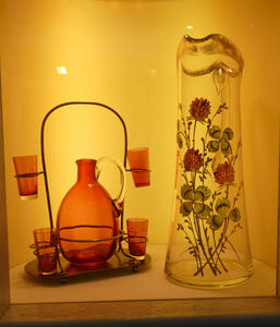 At left, red pitcher and four red glasses. At right, clear vase with flowers painted on it.
