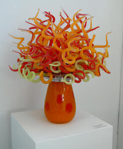 Orange vase. Coming out at the top are twisted strands of glass in green, orange, and red, looking much like Medusa’s hair.