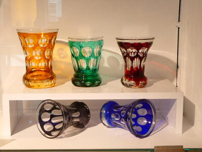 Five drinking glasses in the same style in orange, green, red, blue, and black. All have circular “holes” in the coloring.
