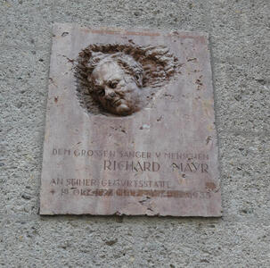 Weathered carving of a man’s head on plaque dedicated to “Dem grossen Sänger u. Mensch Richard Mayer”