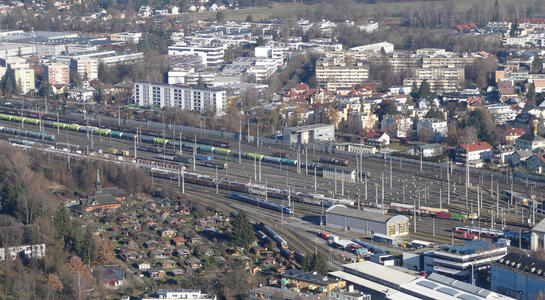City view; houses in foreground, in midground a railway center with a train on one of the tracks; city buildings in background