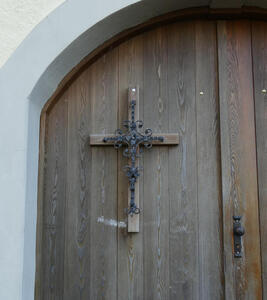 Wooden cross on wooden door. Instead of Jesus, it has intricate metalwork on the cross.