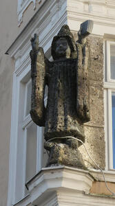 Statue on side of building of man in monk’s robes, hands raised, with a book in one hand.